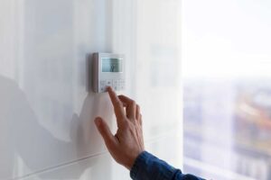A person adjusting a digital programmable thermostat on a living room wall.