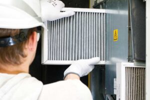 Person replacing a pleated HVAC filter beside a clean return-air grille in a bright home.
