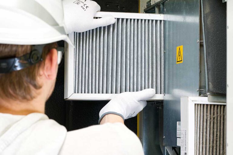 Person replacing a pleated HVAC filter beside a clean return-air grille in a bright home.